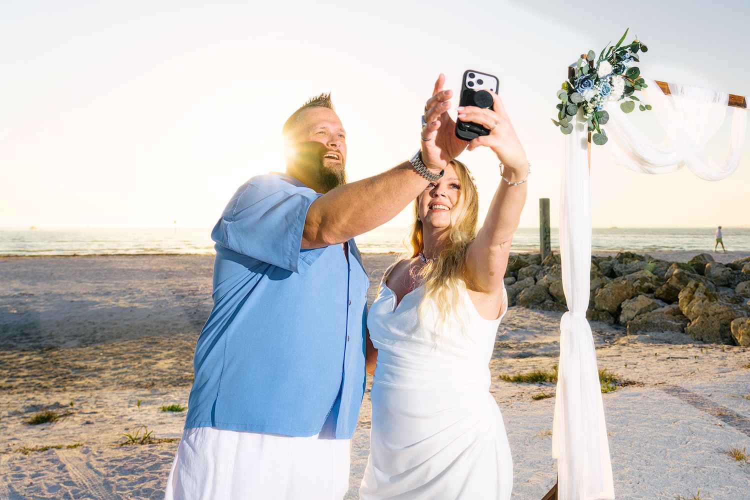 Wedding ceremony setup on a beach with white chairs and floral arrangements.