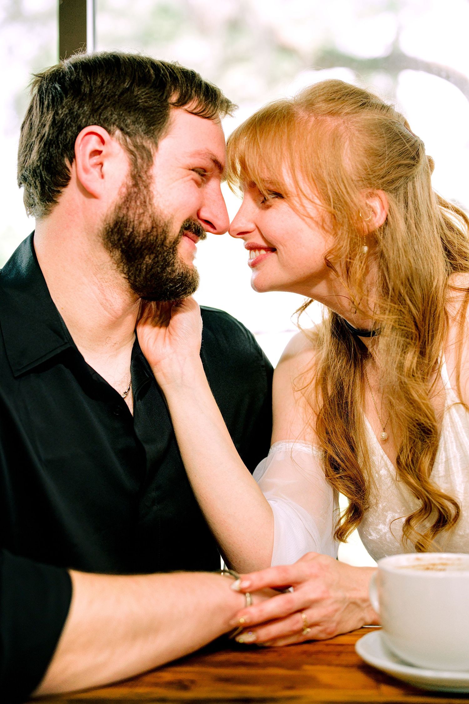 Romantic couple touching foreheads and smiling together at a cafe table with coffee.