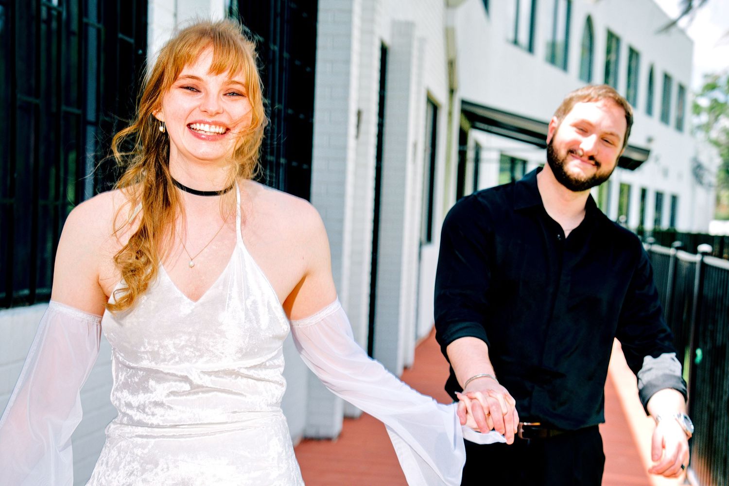 Happy couple holding hands and walking together, woman in white dress and man in black shirt.