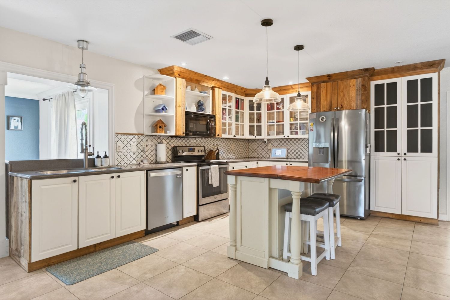 Modern kitchen with stainless steel appliances, white cabinets, center island with seating, pendant lights, and decorative backsplash.