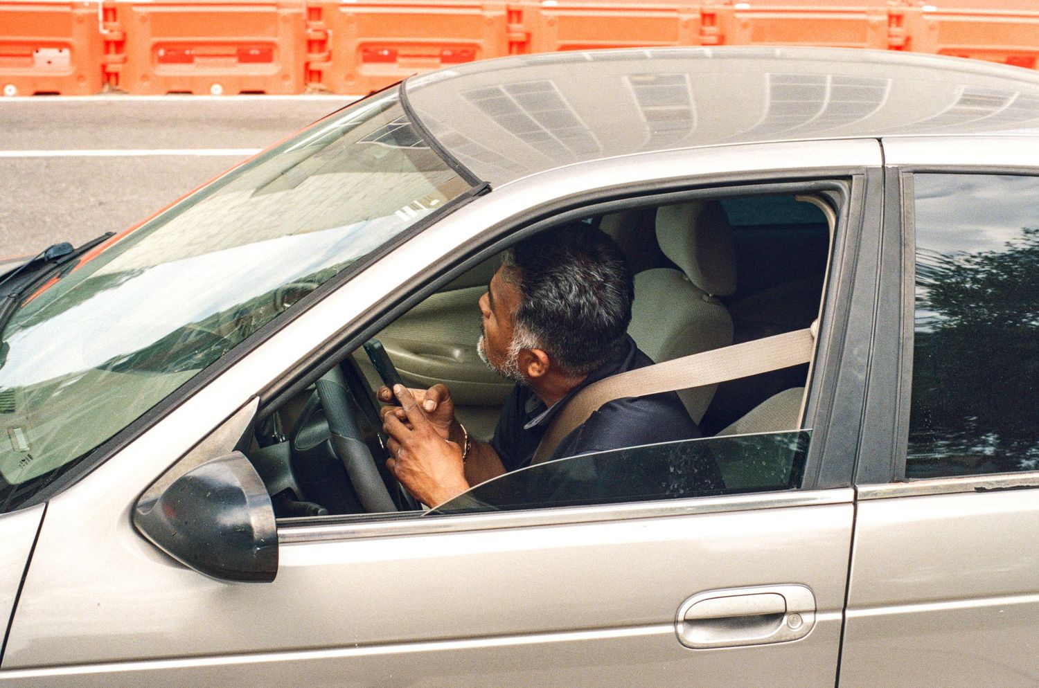 Man talking on phone while driving a silver car, distracted driving concept.