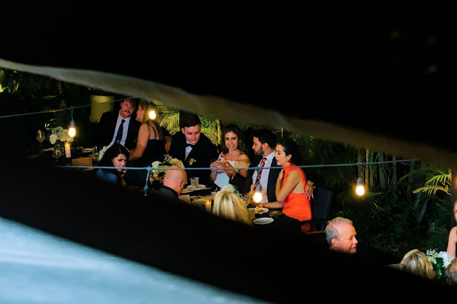 Wedding reception guests mingle under outdoor string lights at night.