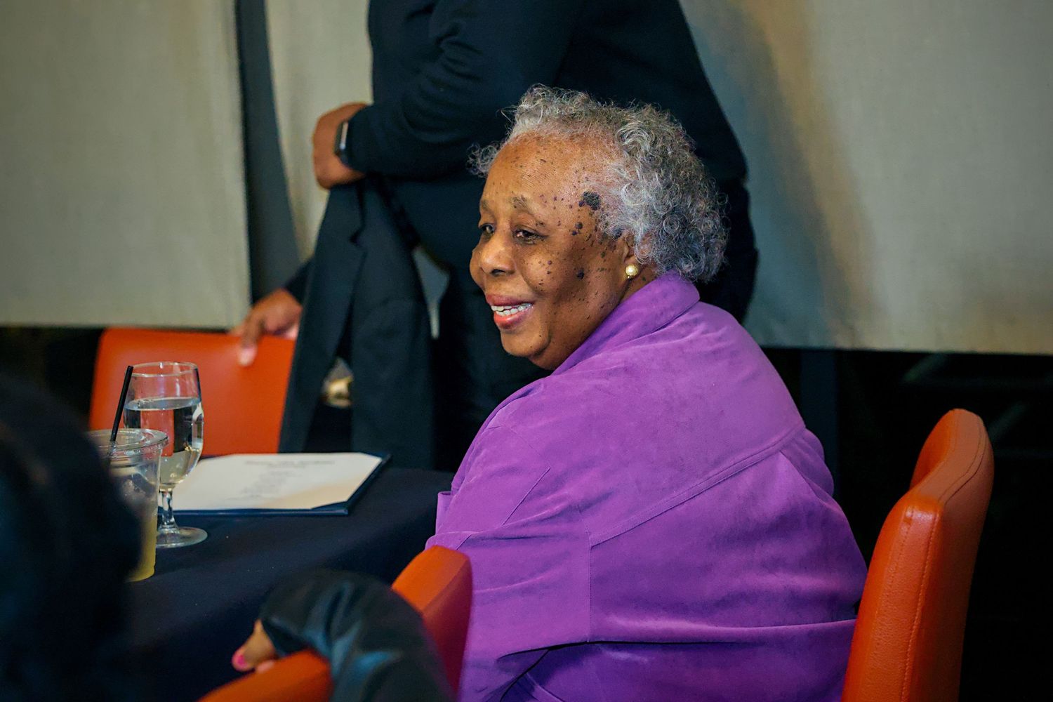 A person wearing a bright purple sweater sits in a red chair during an indoor event.