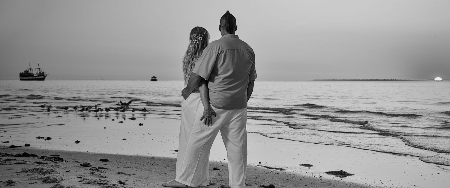 A black and white photo of a couple walking along a beach shoreline.