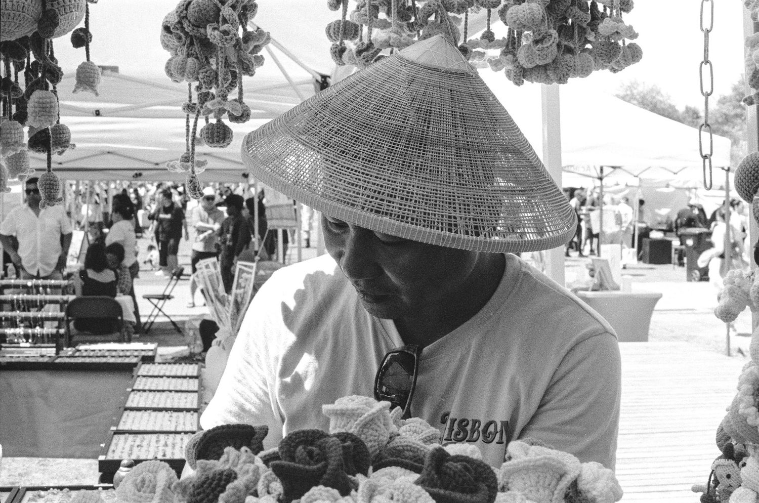 Vendor wearing traditional Asian conical hat selling goods at outdoor market, black and white.
