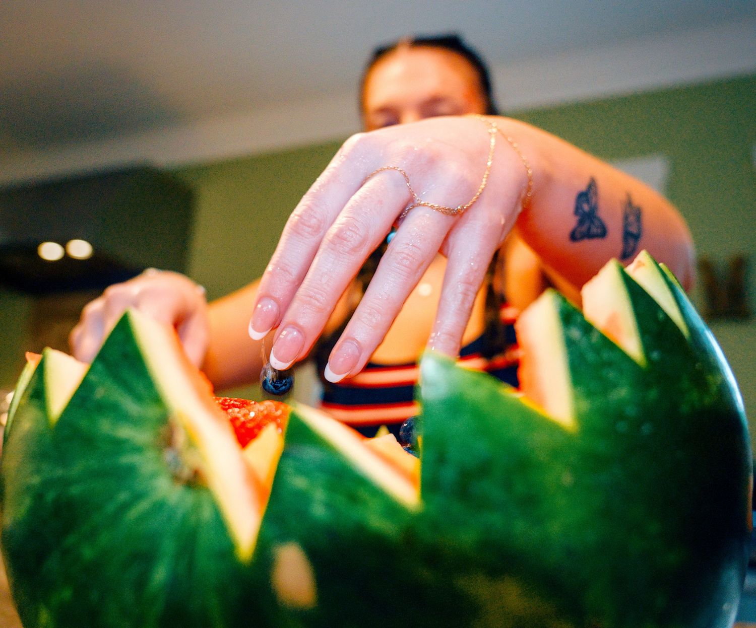 Person with tattoo arranging a decoratively carved watermelon with pointed edges at a dining table.