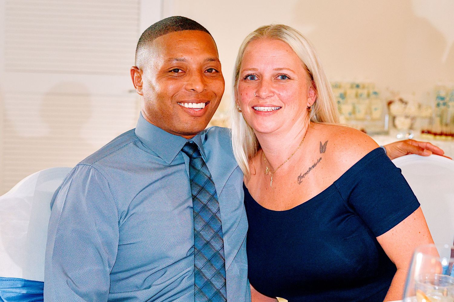 A smiling couple poses together at a formal event, the man in a blue tie and woman in a navy dress.