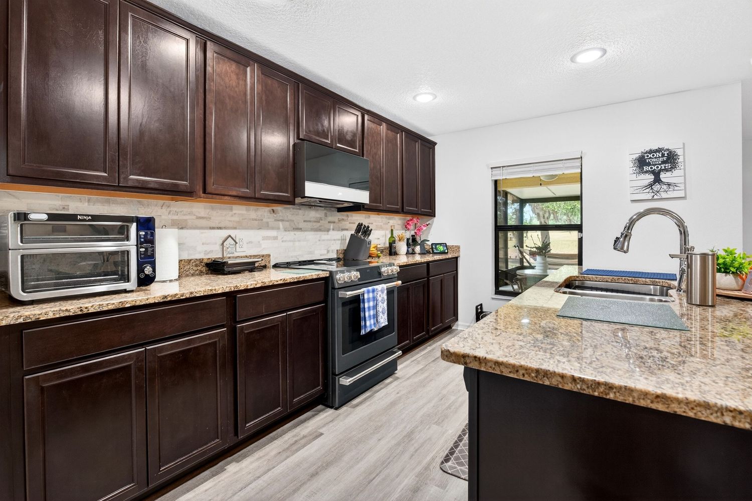 Modern kitchen with dark wood cabinets, granite countertops, stainless steel appliances, and light hardwood floors.