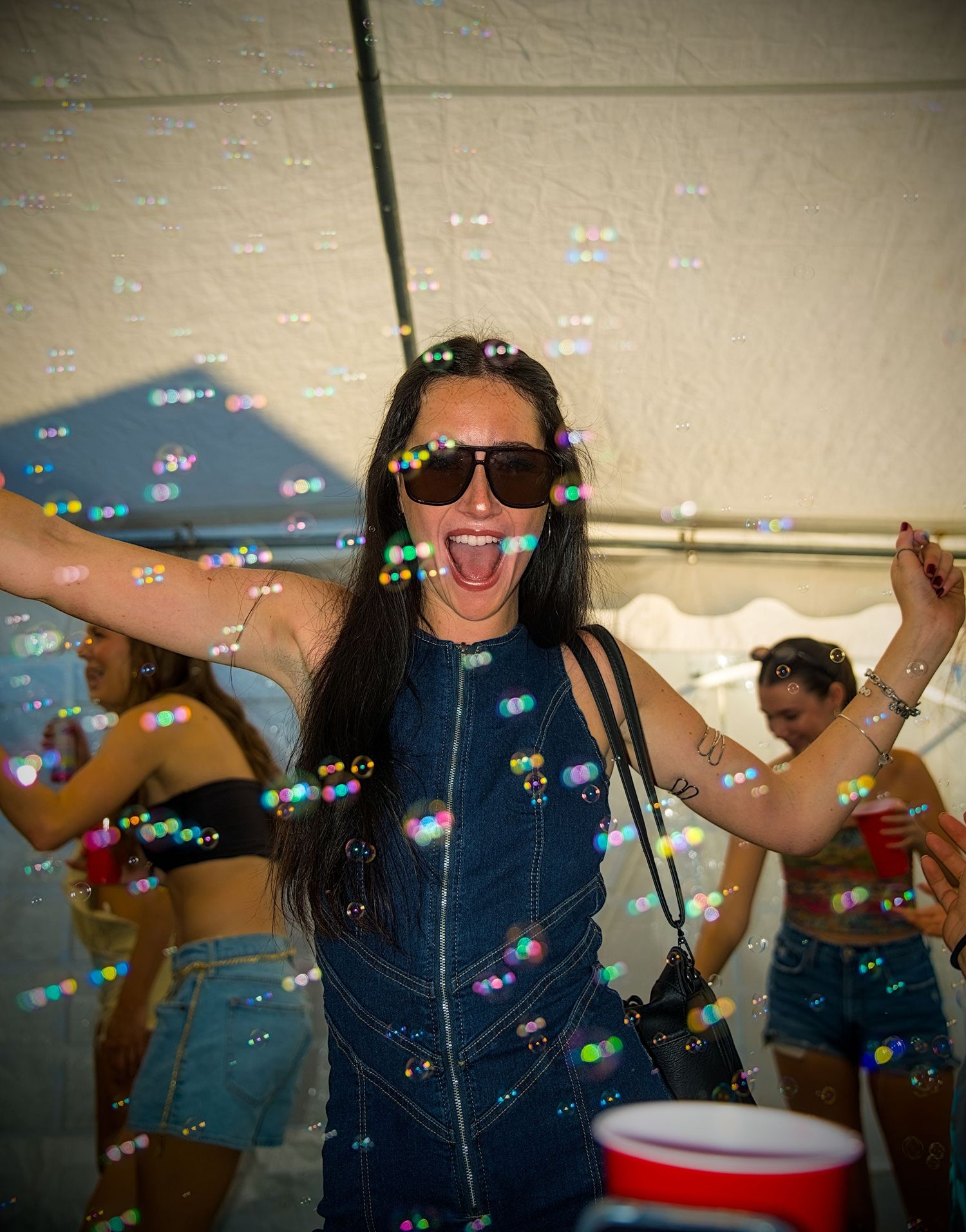 Someone in denim overalls dances energetically at a party with soap bubbles floating through the air.