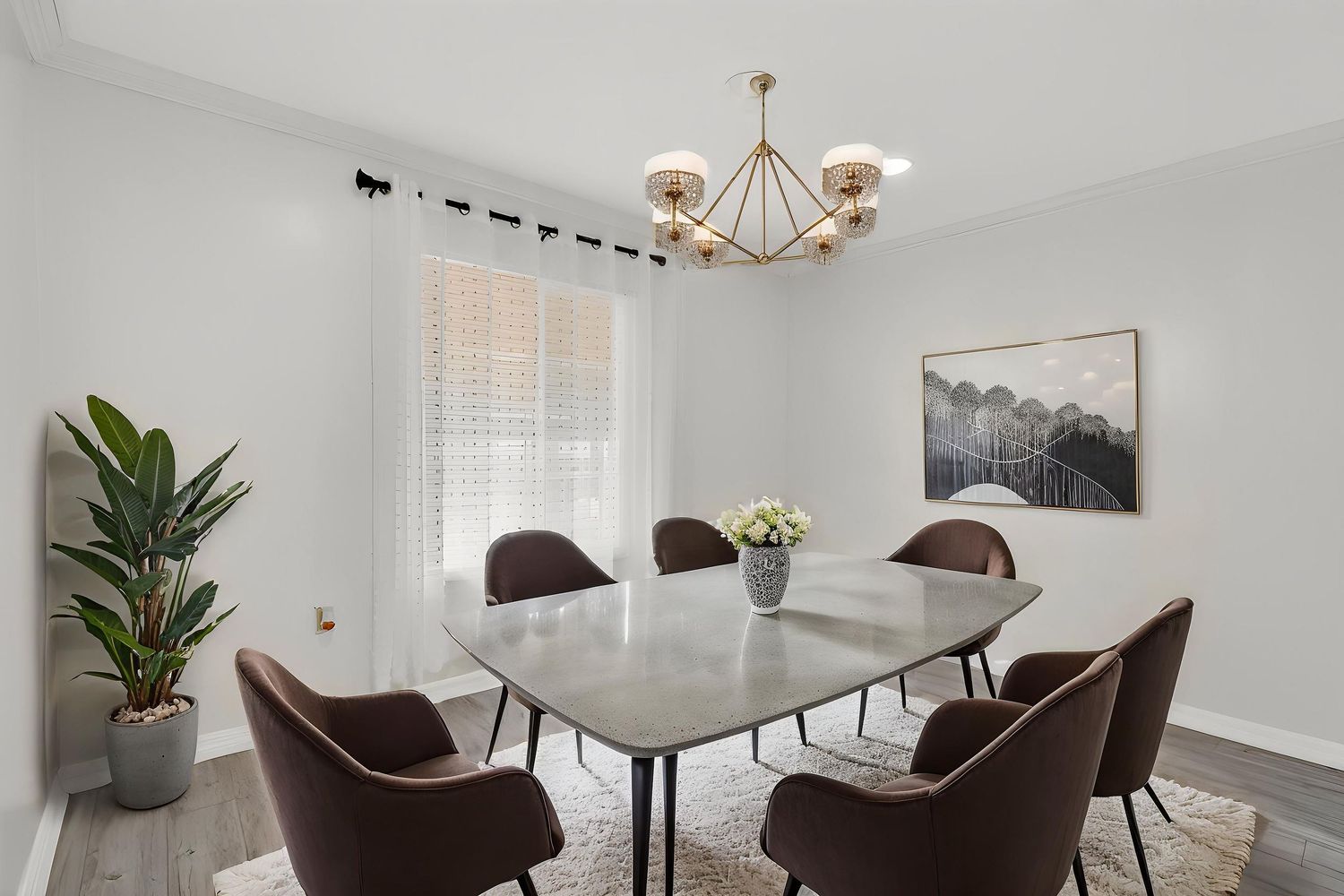 Modern dining room with marble table, brown velvet chairs, brass chandelier, and black and white mountain artwork.