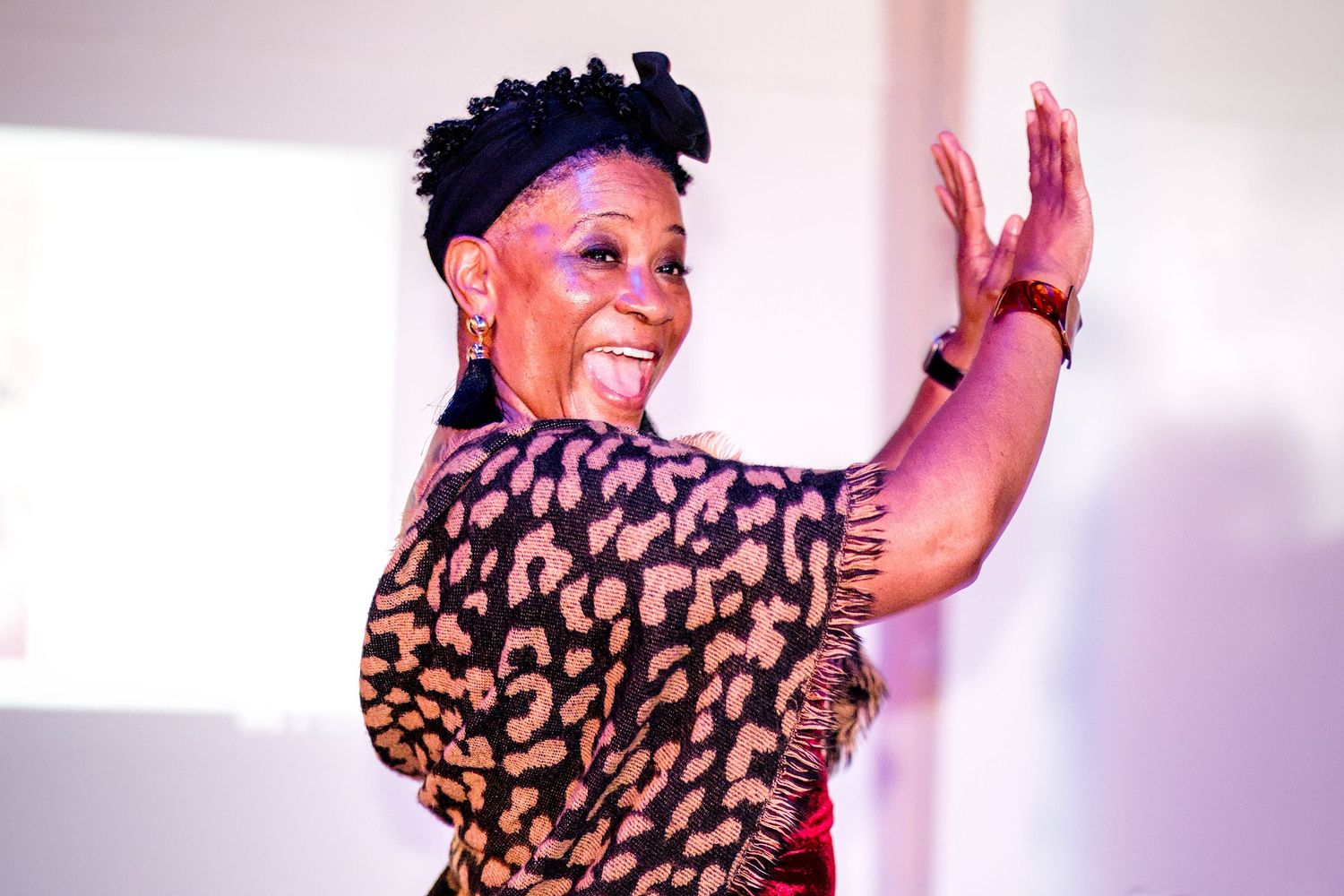 Energetic Black woman in a leopard print top waves her hand while presenting at an indoor event.