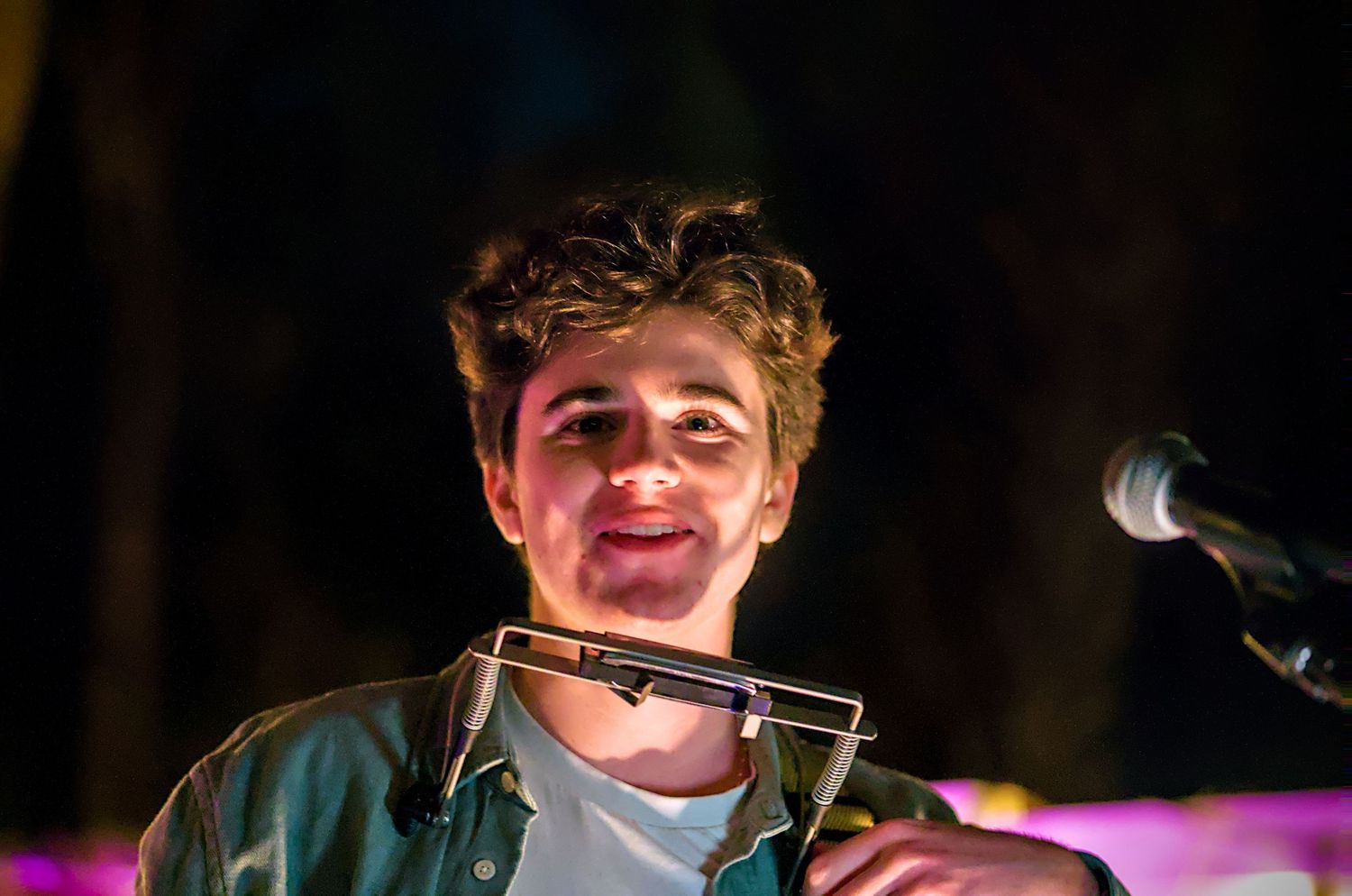 A performer sings into a microphone on stage under colorful lighting during a live show.