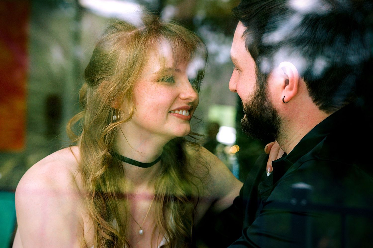 A smiling woman with long blonde hair and a man with a beard share a romantic moment gazing at each other.