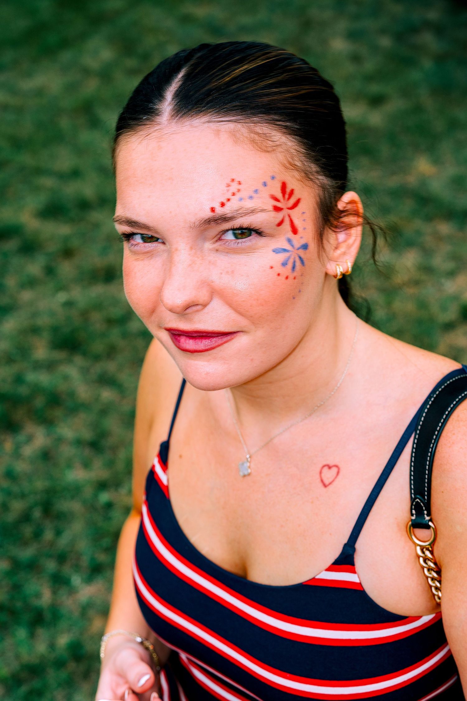 Young woman with face paint designs and a heart tattoo on chest, wearing striped top outdoors.