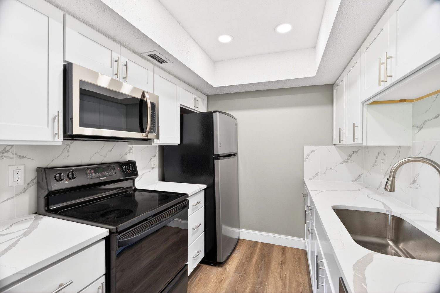 Modern white kitchen interior with stainless steel appliances, dark countertops and recessed lighting.