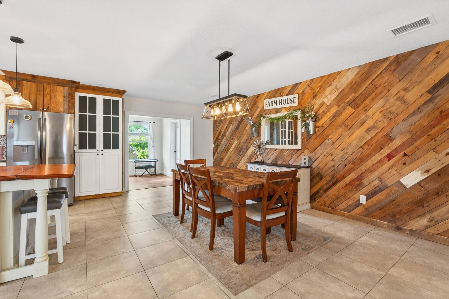 Dining area with rustic reclaimed wood accent wall, wooden table, chairs, and modern pendant light over tile floors.