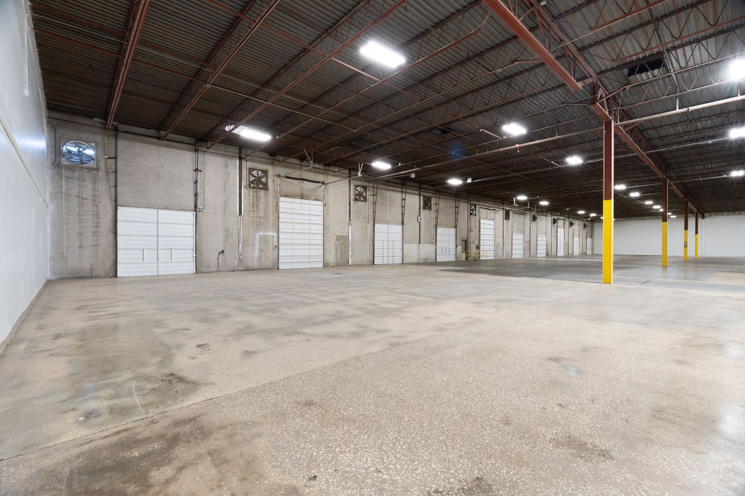 Large empty industrial warehouse interior with concrete floors and exposed ceiling showing multiple connected spaces.
