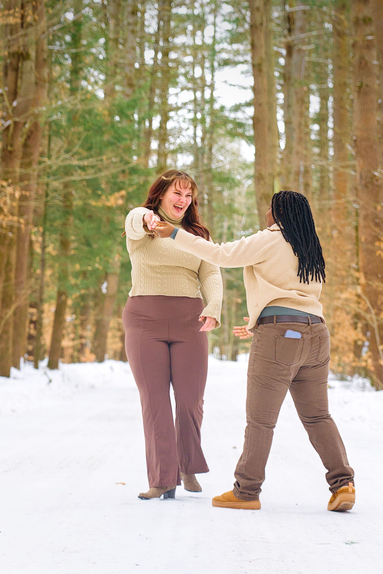 Two people playfully throwing snowballs at each other in a snowy winter forest setting.