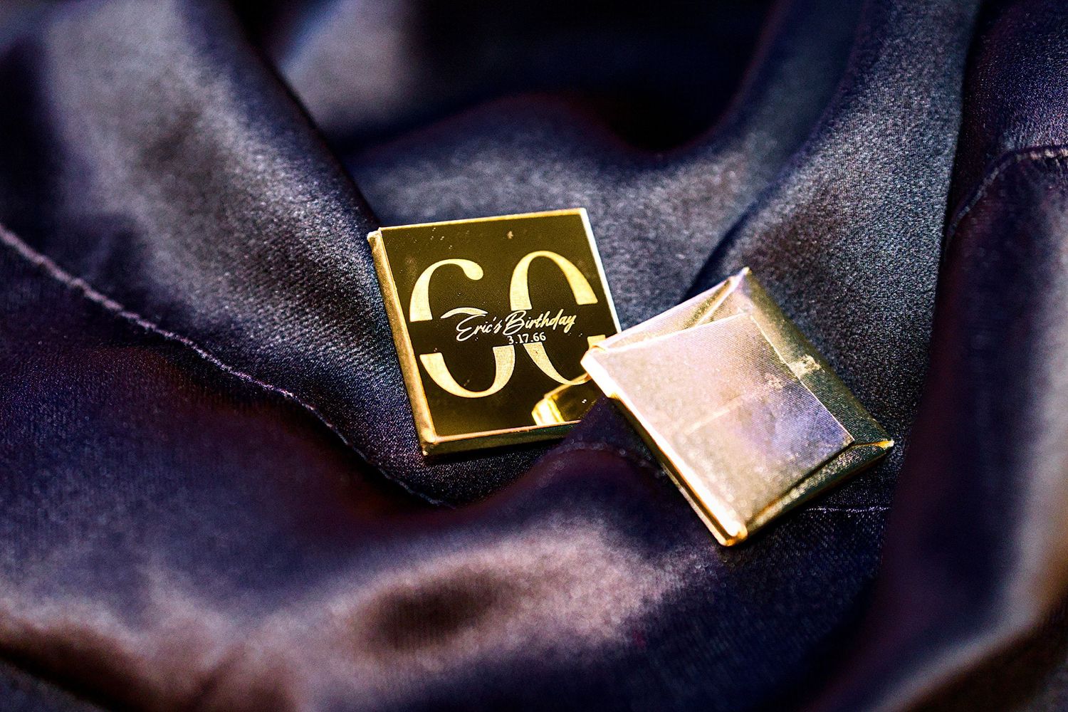 Gold Givenchy cufflinks with engraved logo resting on blue satin fabric.