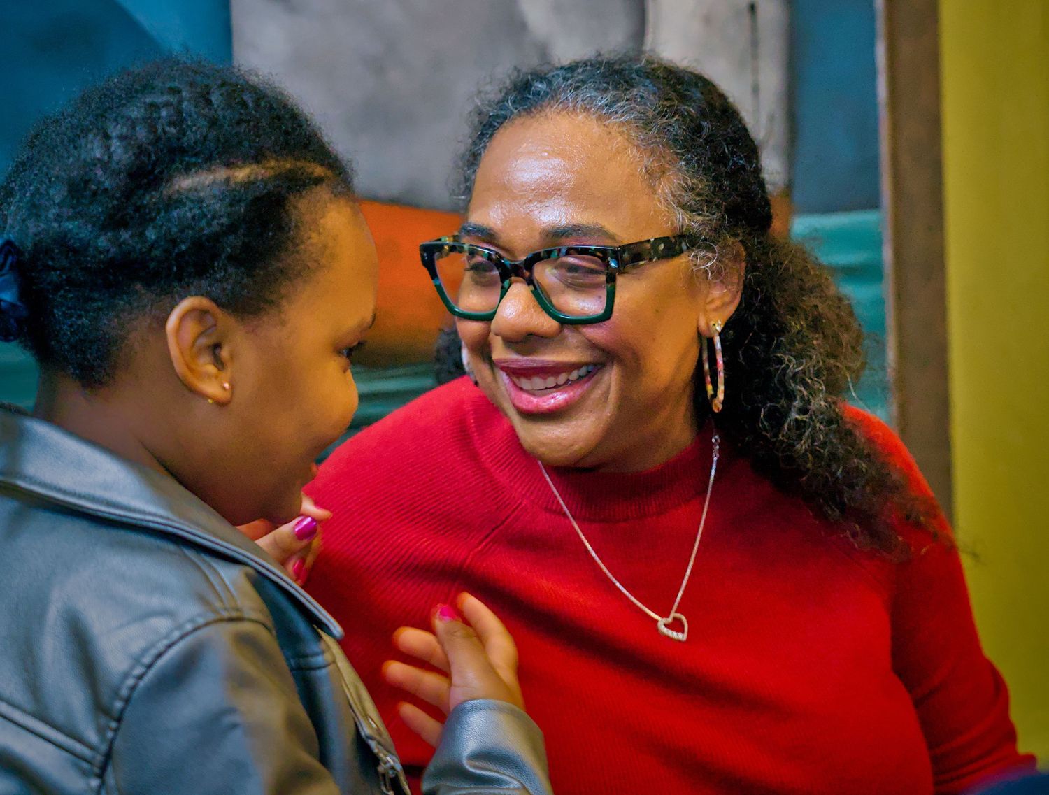 Two people share a joyful moment while wearing glasses and a red sweater in an intimate conversation.