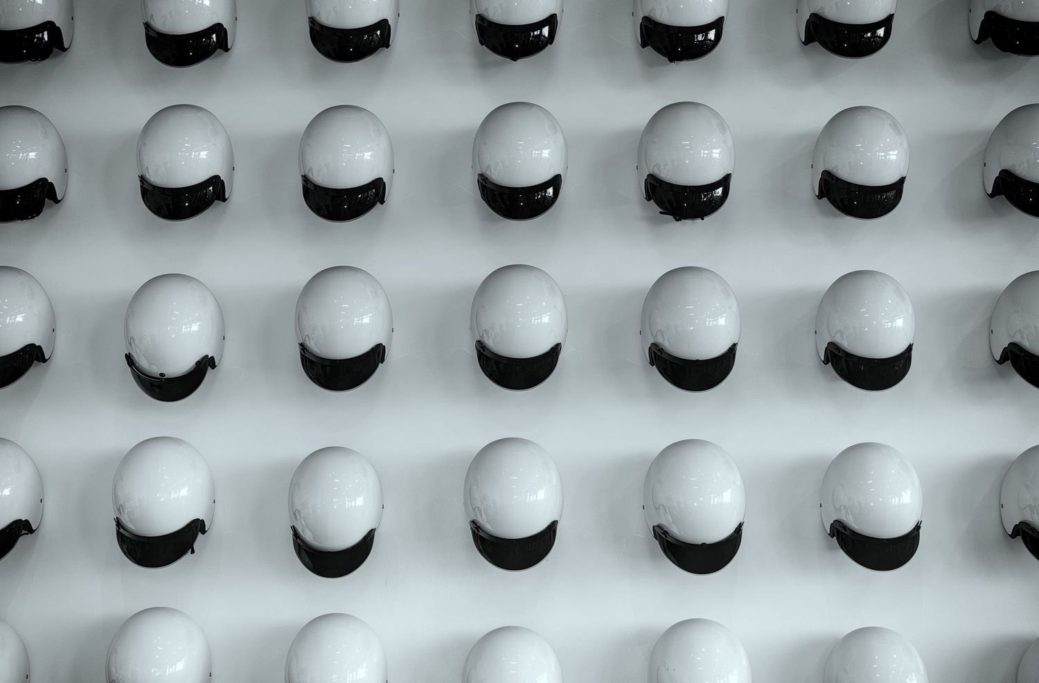 Rows of white LEGO minifigure heads with black visors arranged in a uniform grid pattern on a light gray surface.