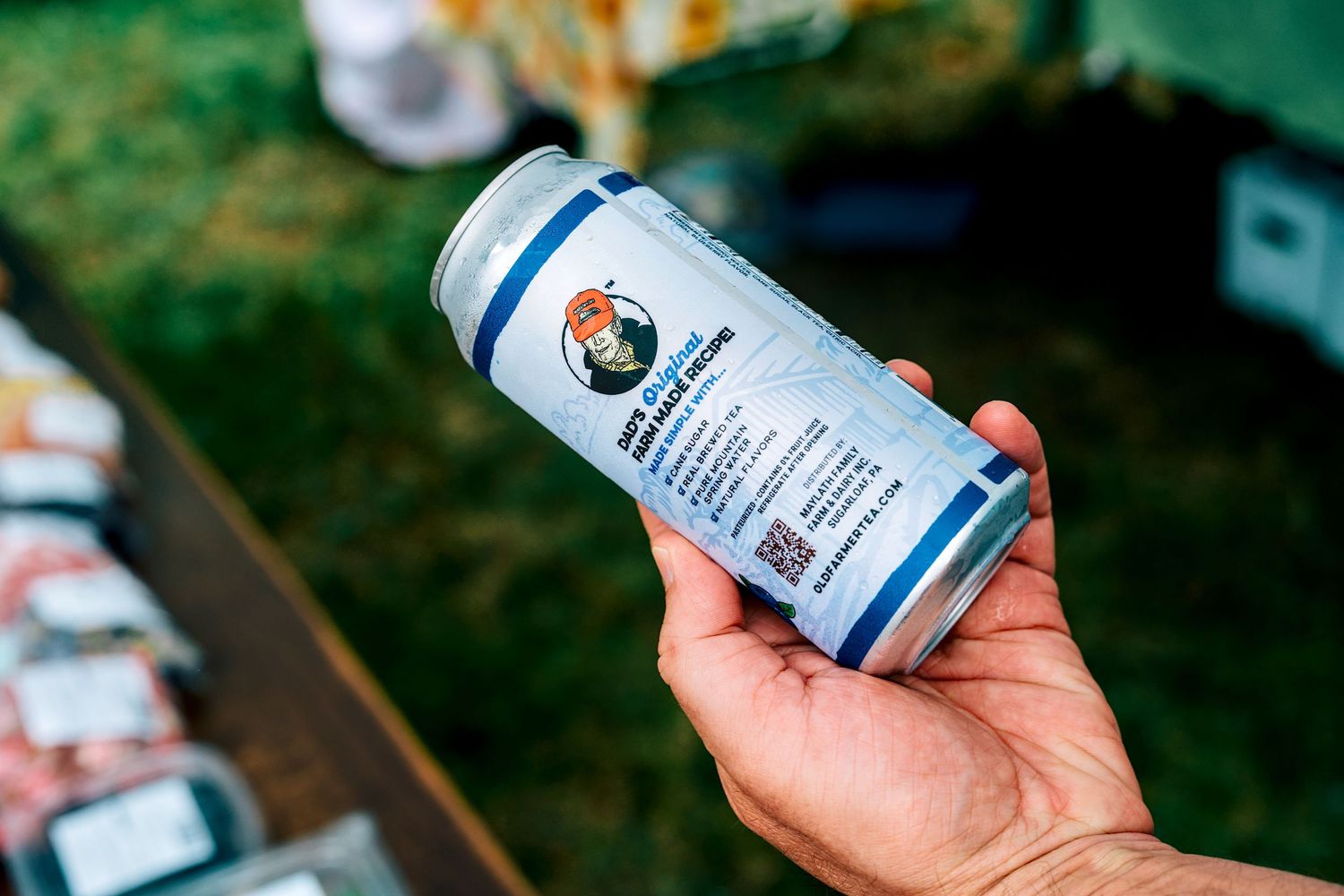 Hand holding a craft beer can with a colorful label outdoors at a market event.