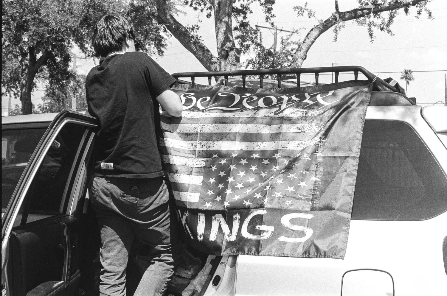 Man attaching an American flag to a car roof rack in a black and white outdoor photo.