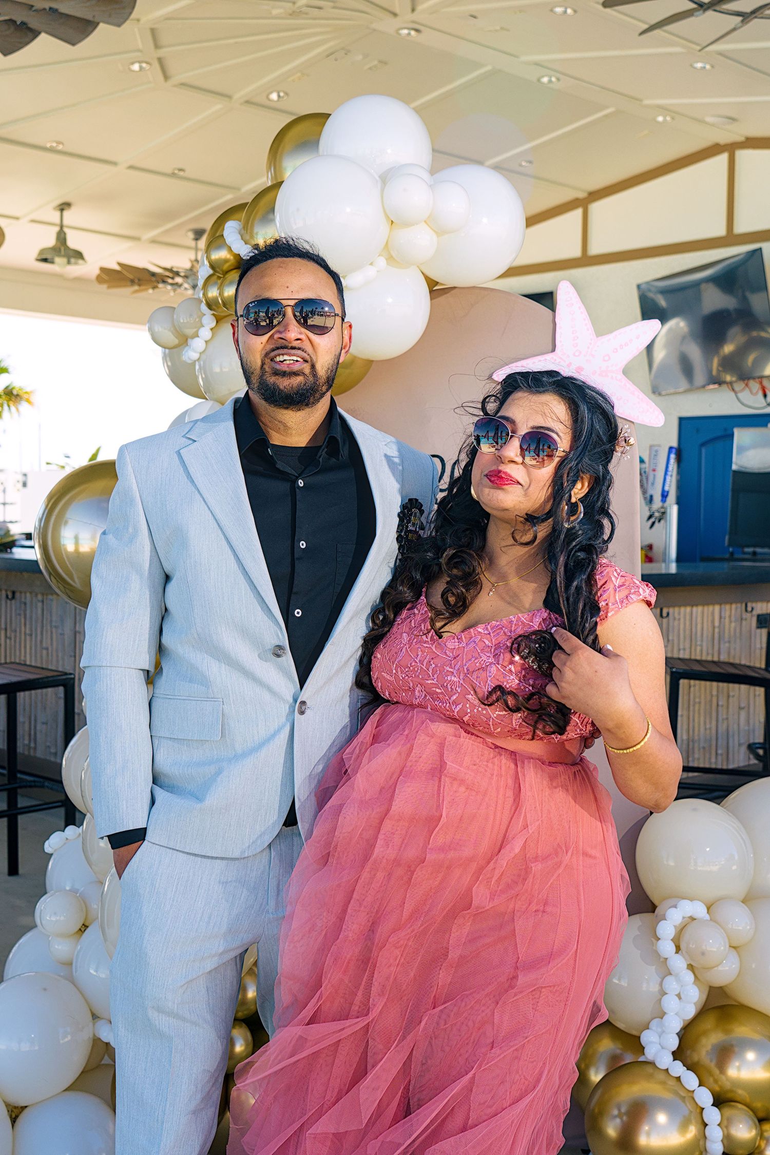 A couple poses together at an elegant event with white and gold balloon decorations.