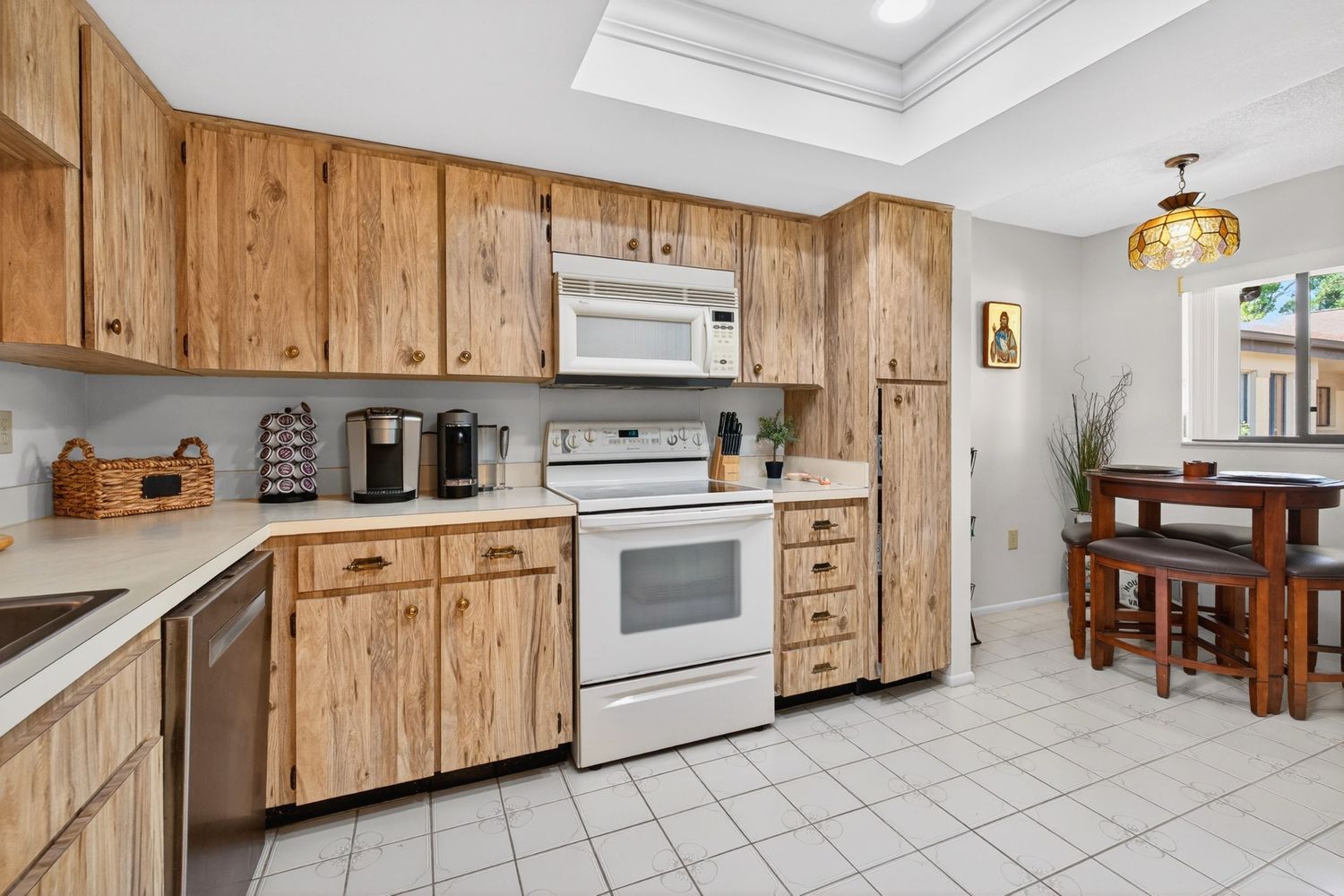 Kitchen with wood cabinets, white appliances, tile floors, and a dining area visible in the background.