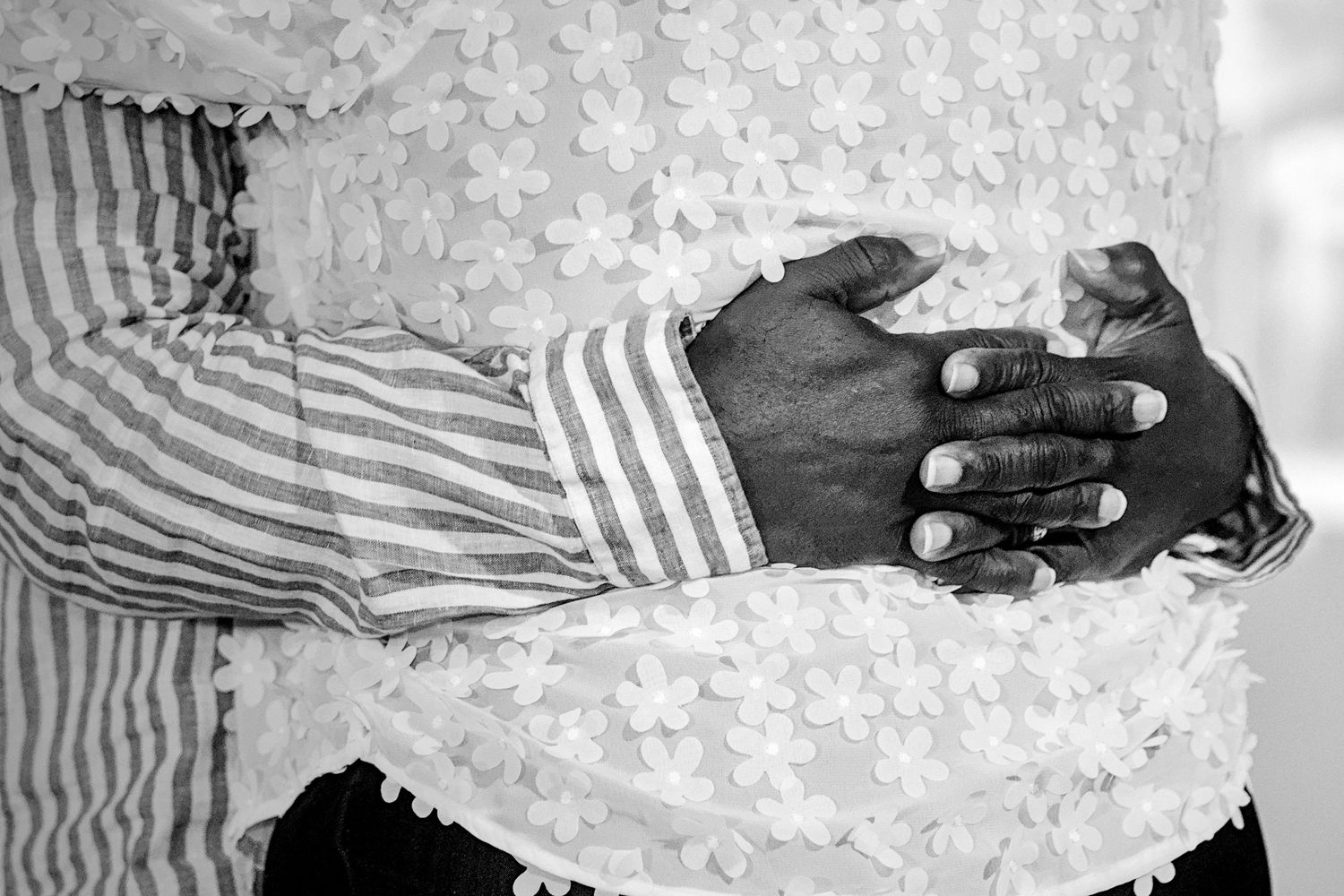 Black and white photo of two people clasping hands, one wearing a striped shirt and the other in floral lace.