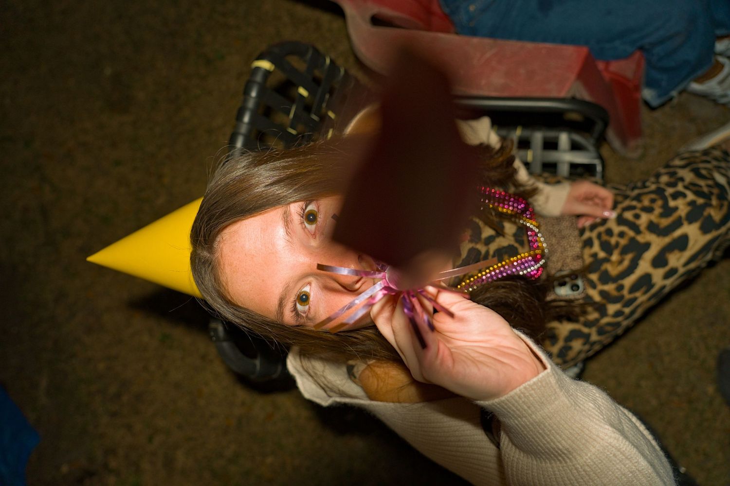 Woman wearing yellow party hat blowing a noisemaker at a birthday celebration party indoors.