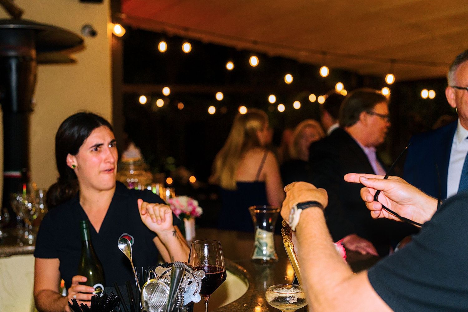 Wedding party mingling at a dimly lit reception with decorative string lights.