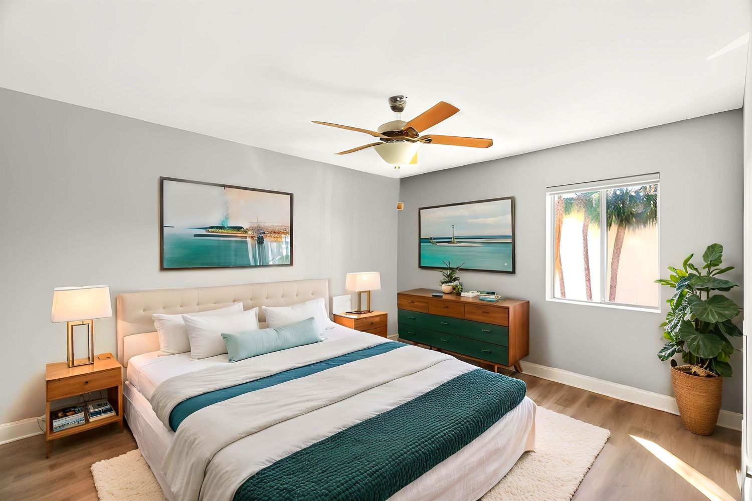 Modern bedroom interior with white bedding, teal accents, ceiling fan, and natural light from windows.
