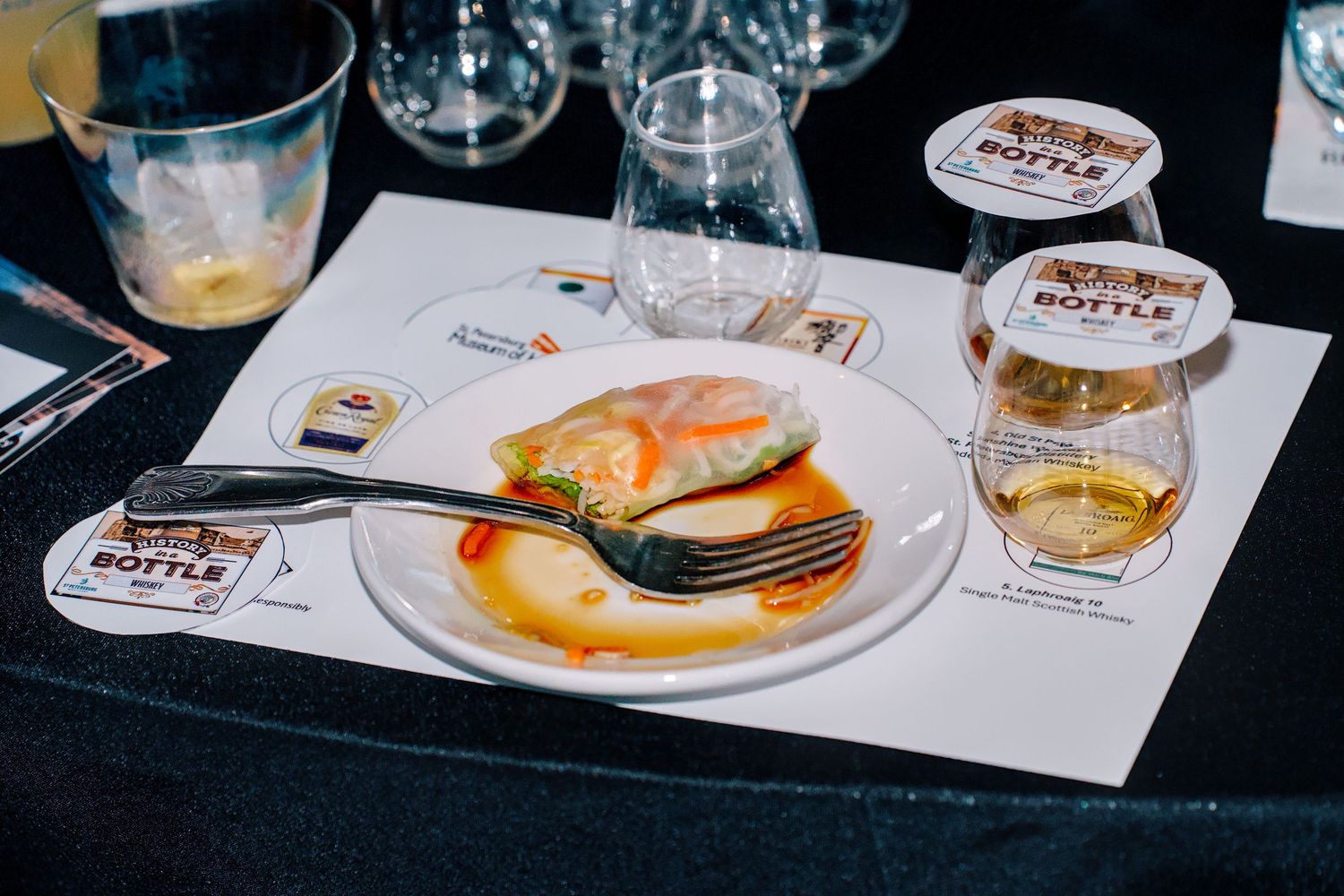 A gourmet dish with salmon and sauce on a white plate, paired with whisky glass at a tasting event.