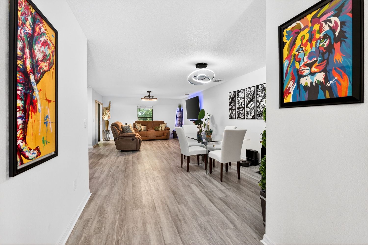 Modern open-plan living and dining room with hardwood floors, white walls, colorful artwork, and stylish furniture.