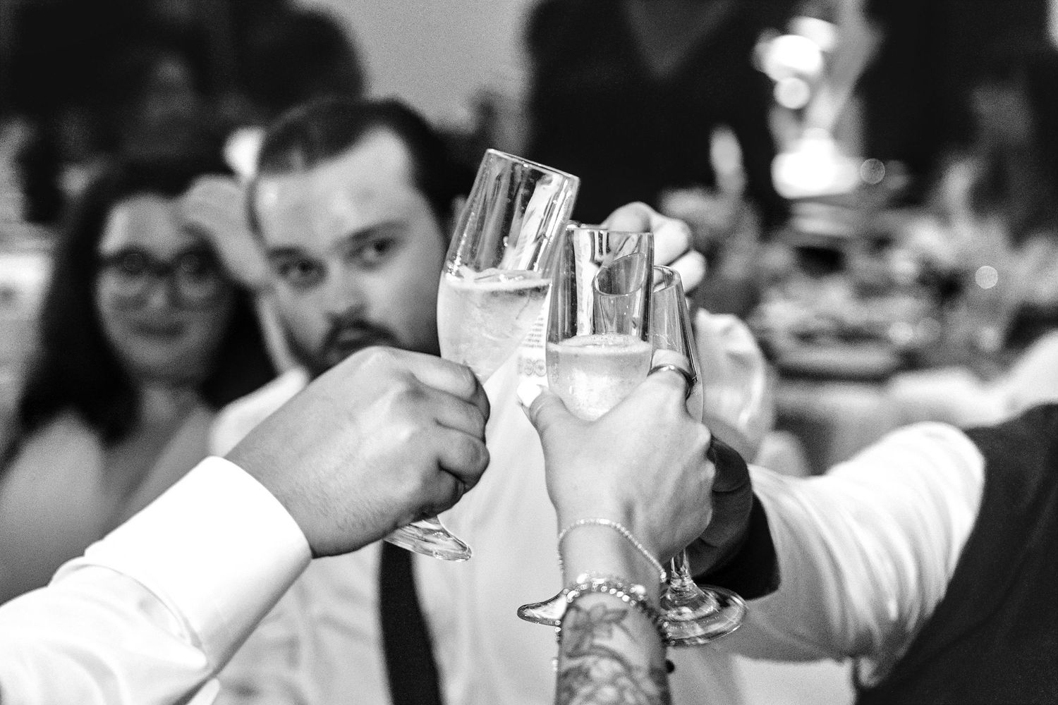 Guests clinking champagne glasses in a toast at a wedding reception in black and white.