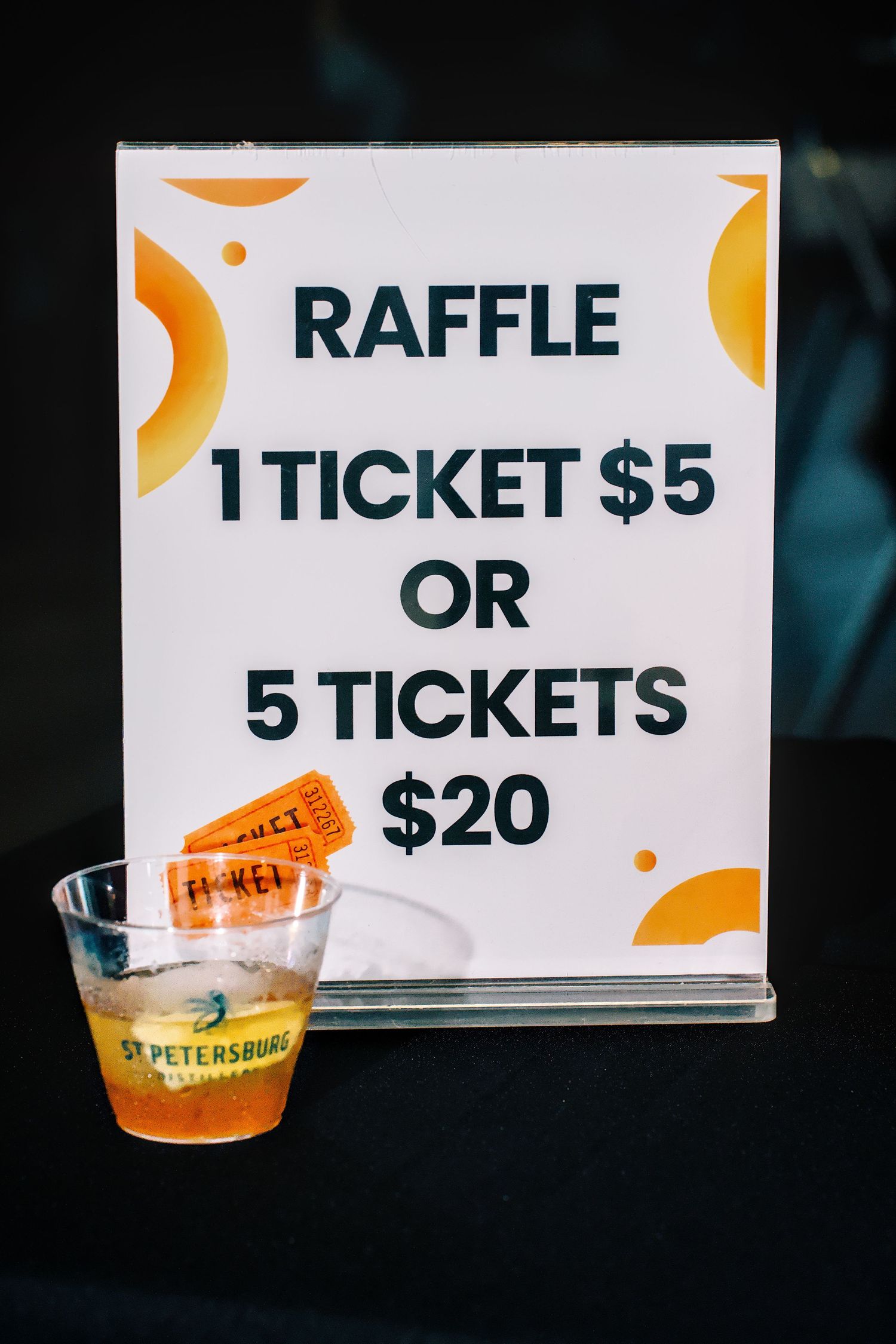 Raffle ticket sign offering 1 ticket for $5 or 5 tickets for $20 with orange tickets in a cup.