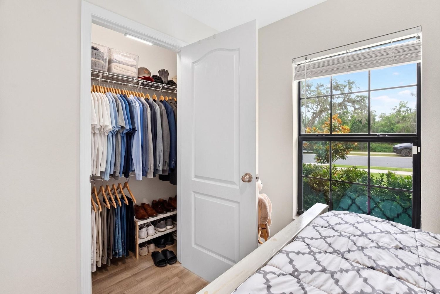 Bright bedroom with a walk-in closet featuring organized shelving and a large window overlooking lush greenery.