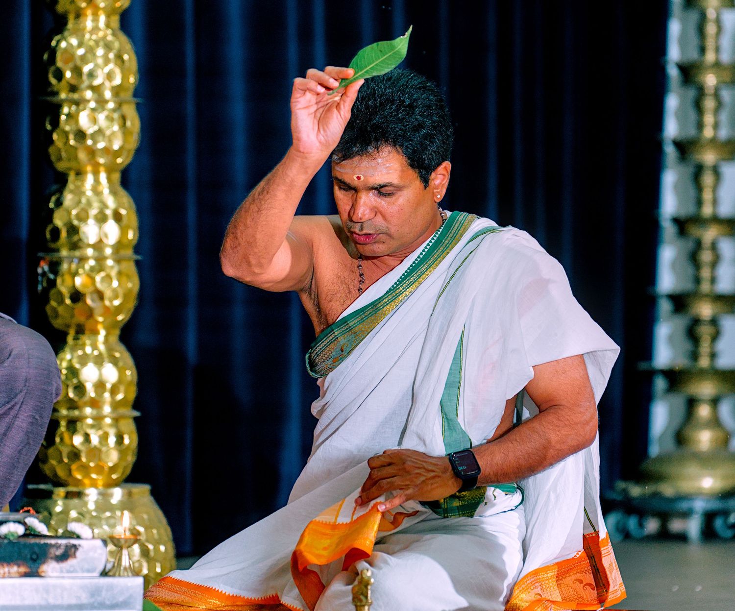 Hindu priest performing a traditional ritual holding a leaf during a religious ceremony.