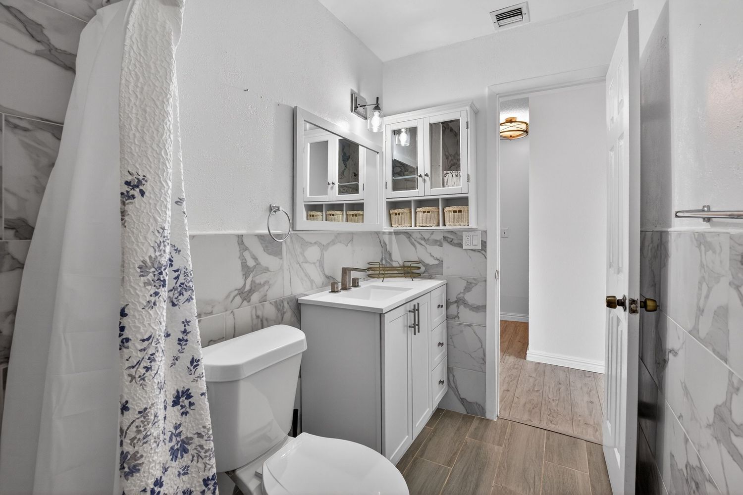 Modern bathroom interior with marble walls, white fixtures, and purple floral accents creates an elegant spa-like atmosphere.