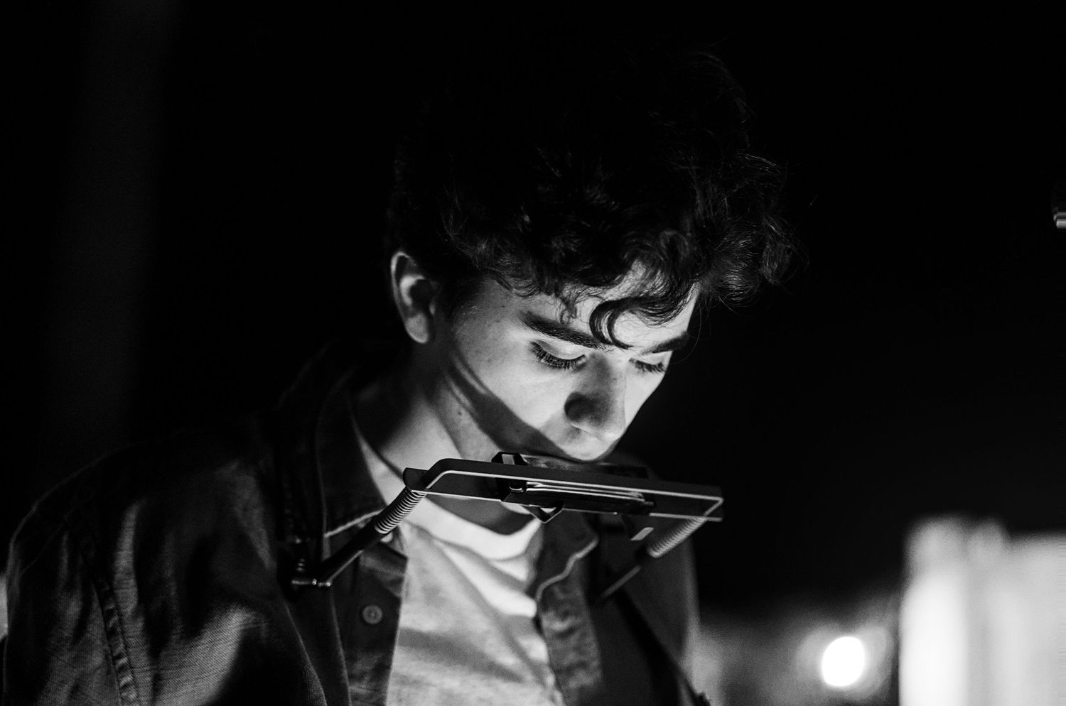 Black and white photo of a young man looking down at a harmonica mounted on a neck holder.