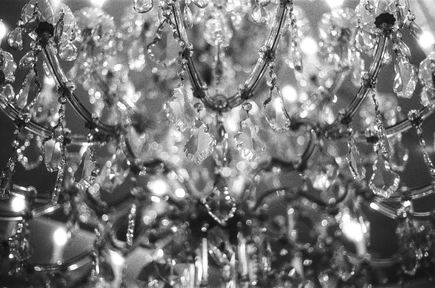 Black and white close-up of a sparkling crystal chandelier with elegant glass droplets and ornate metalwork.