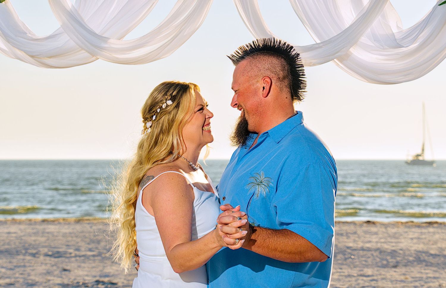 Couple embracing on a rocky beach at sunset with ocean waves in the background.