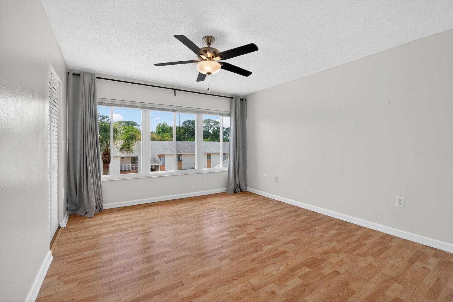 Modern living room with hardwood floors, ceiling fan, and large windows letting in natural light.