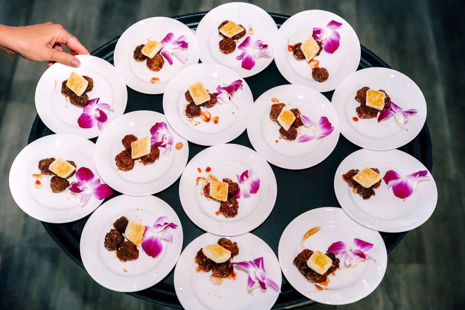 Elegant white plates with gourmet desserts garnished with purple orchids and caramel sauce served on a round tray.