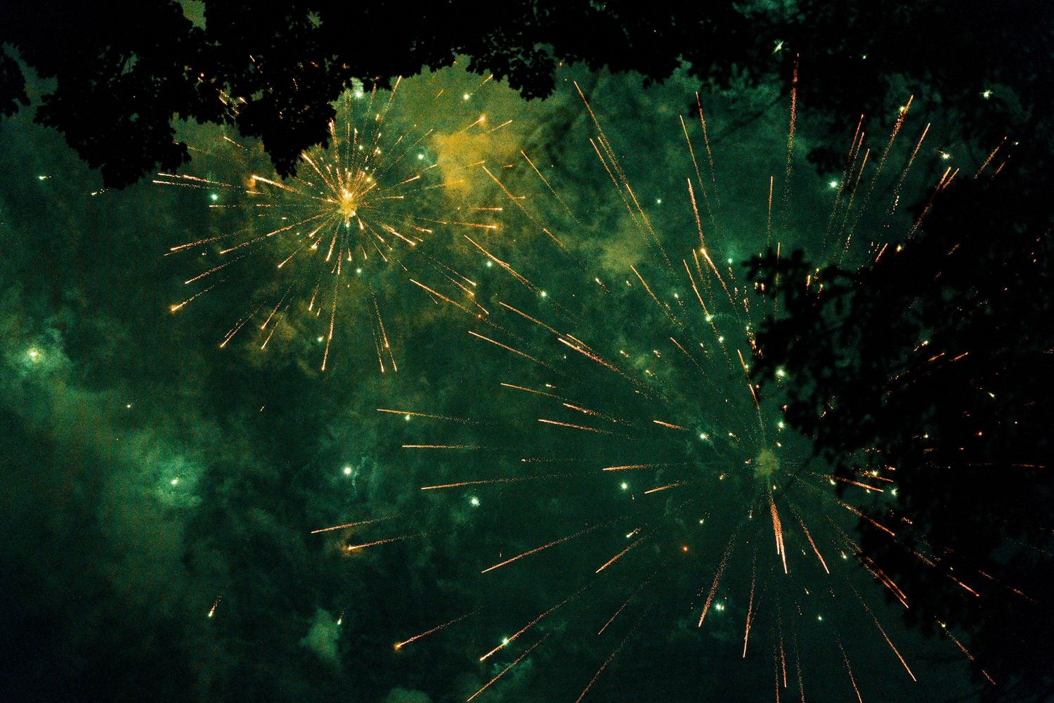 Green and gold fireworks exploding against a dark night sky with glowing emerald smoke clouds.