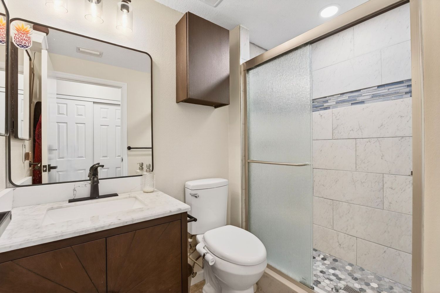 Modern bathroom with dark wood vanity, marble countertop, walk-in glass shower with tile surround, and white toilet.