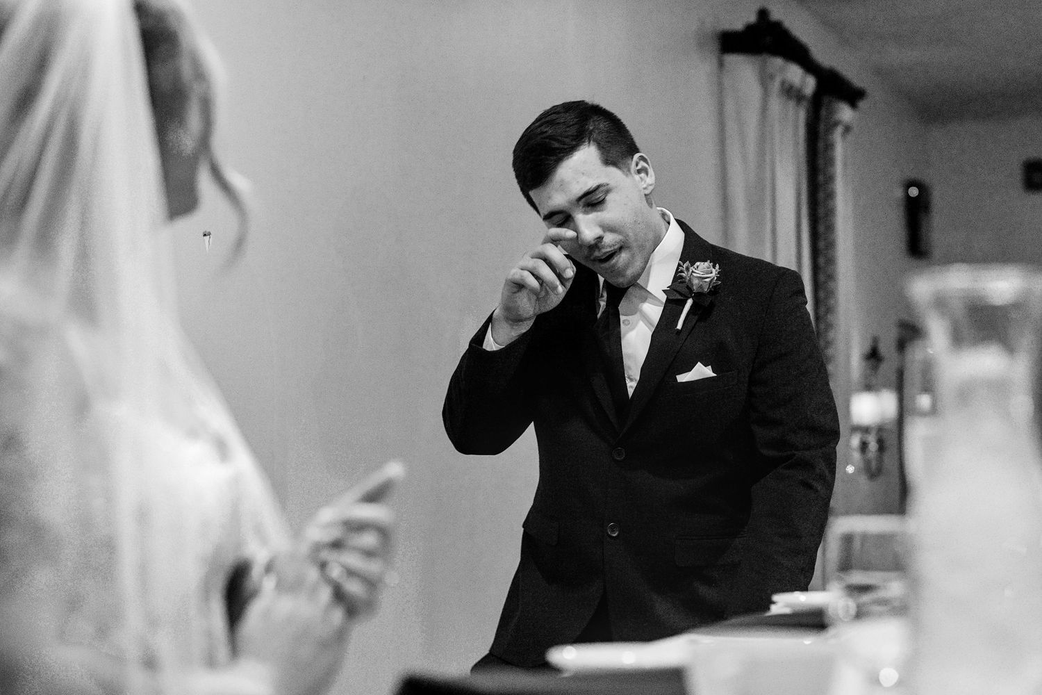 Emotional groom wiping tears during wedding ceremony in black and white photo.