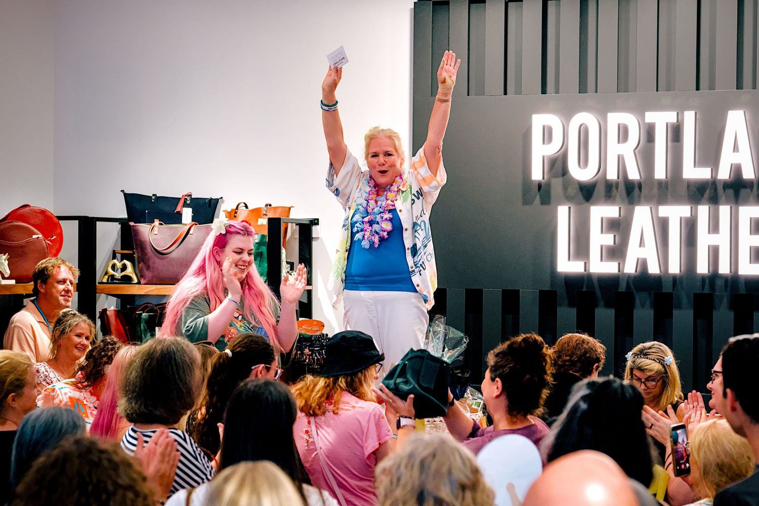 Excited woman raises arms at Portland Leather event surrounded by cheering crowd.