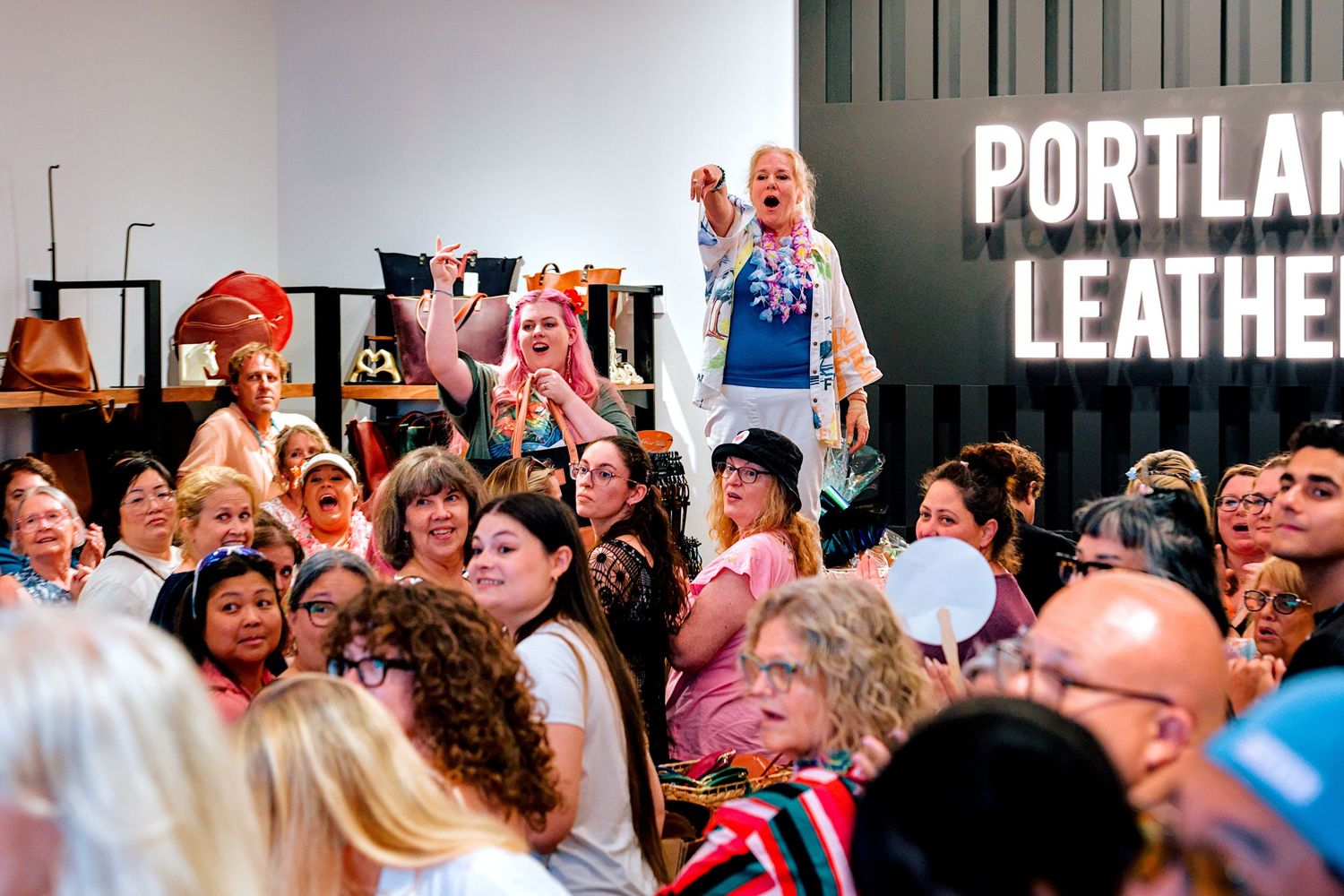 Excited crowd at Portland Leather event, with woman raising fist in celebration among diverse attendees.